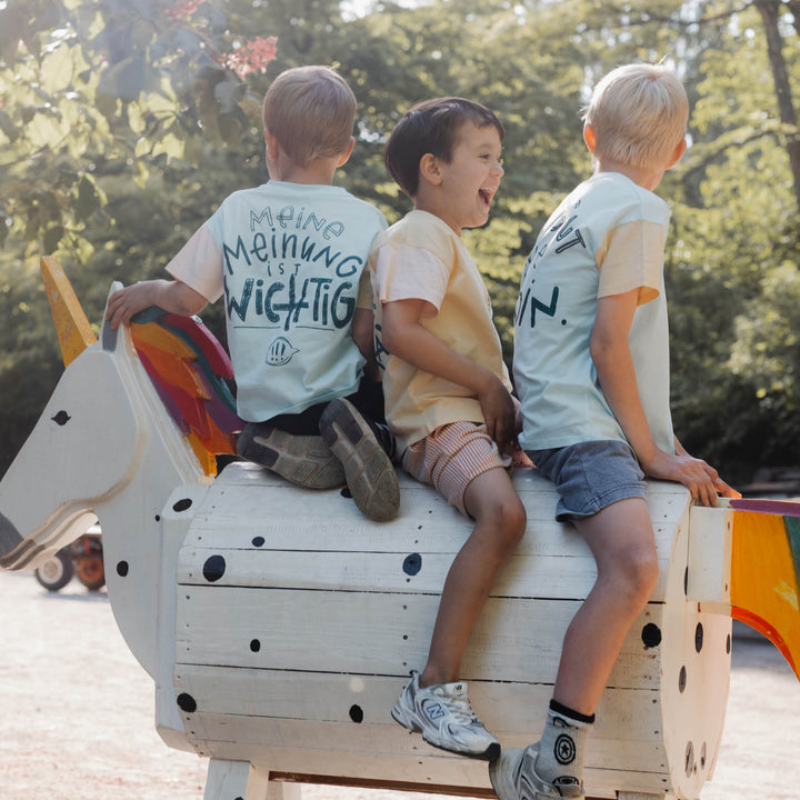Drei Kinder mit Mira Shirts sitzen auf einem Holzpferd