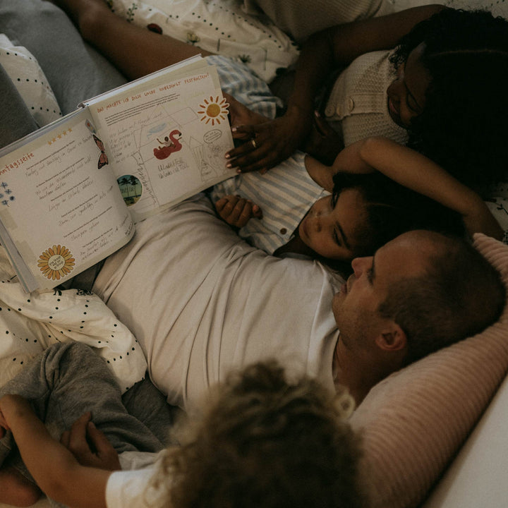 Familie liest gemeinsam im Bett - Eltern mit zwei Kindern schauen in das Buch