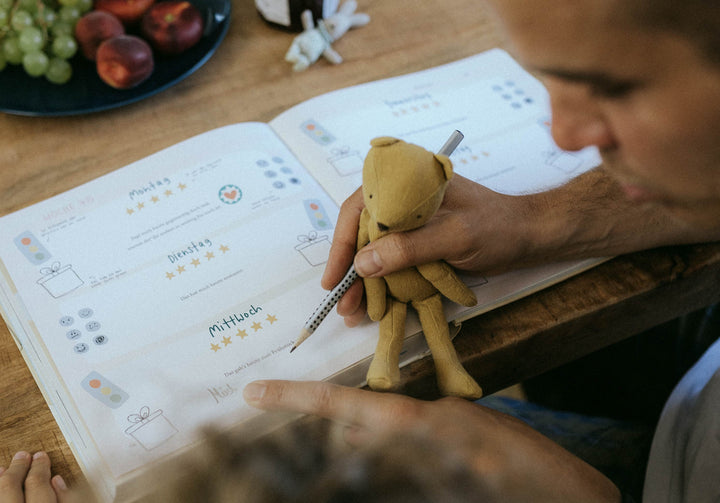 Kind füllt Wochenplaner aus und hält dabei gelbe Stoffpuppe mit Stift in der Hand
