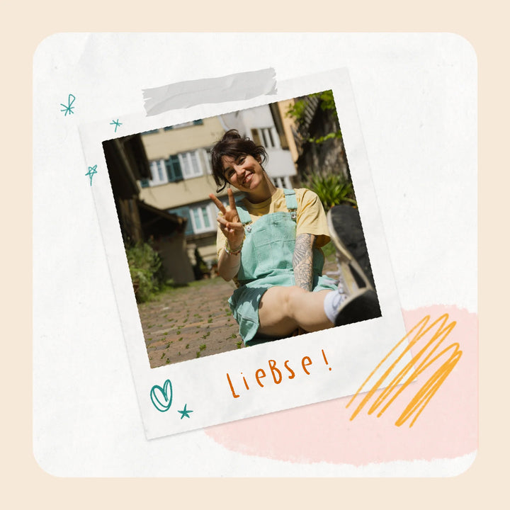 "Polaroid-ähnliches Foto von Mira in türkiser Latzhose und gelbem T-Shirt, die lächelnd ein Peace-Zeichen zeigt. Darunter steht in orangefarbener Handschrift &